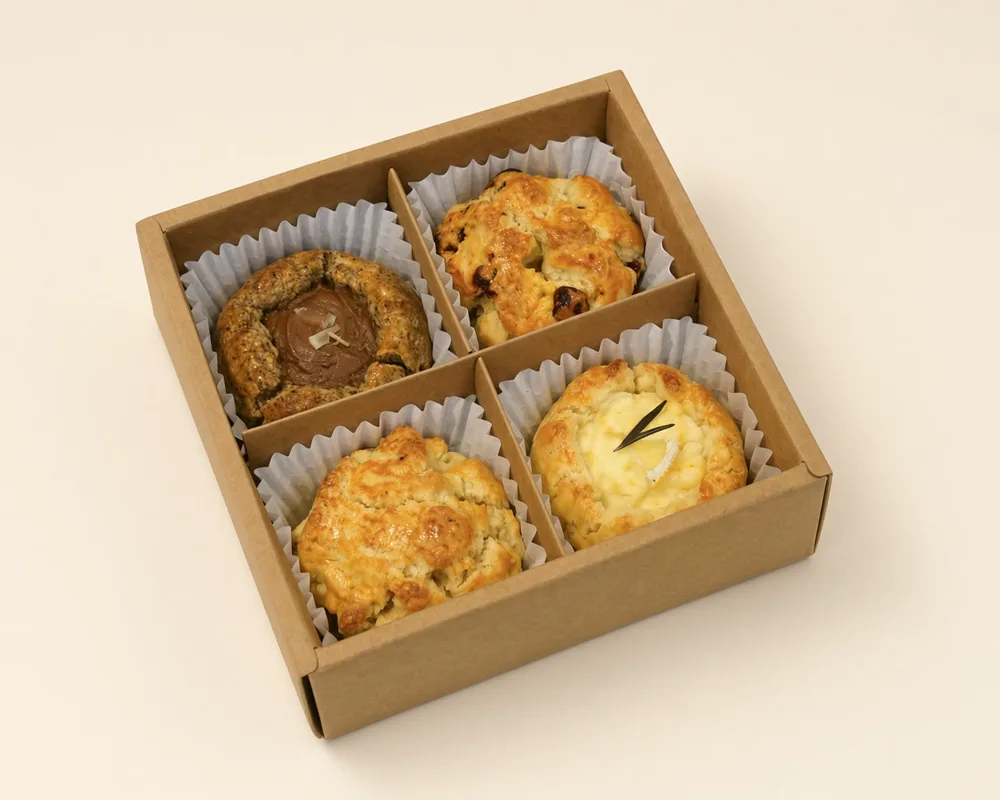 An open kraft SCOF gift box holding four scones, one flavour in each compartment.