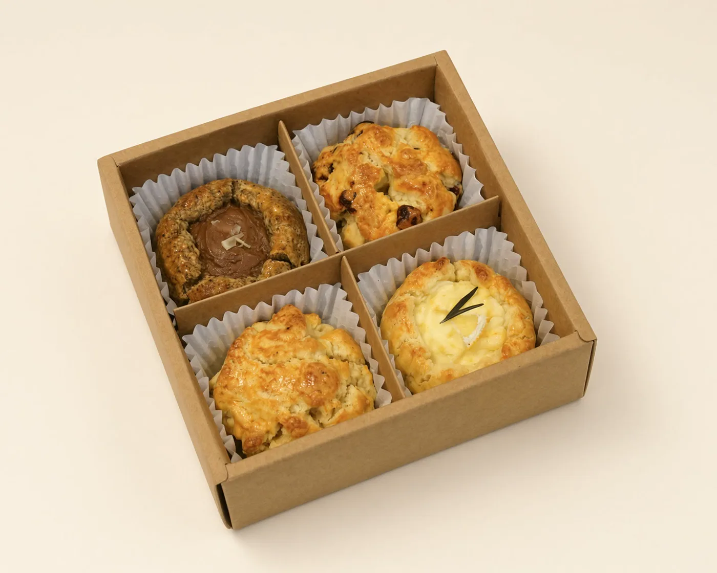 An open kraft SCOF gift box holding four scones, one flavour in each compartment.