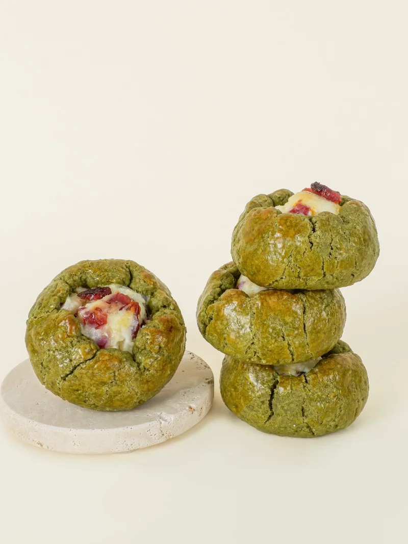 Four Matcha scones, green dough with a cream cheese and cranberry centre — one open on a stone coaster, three stacked.