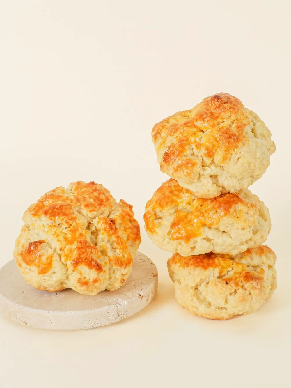 Four Original scones on a cream backdrop, tops glazed golden — one on a stone coaster, three stacked beside it.